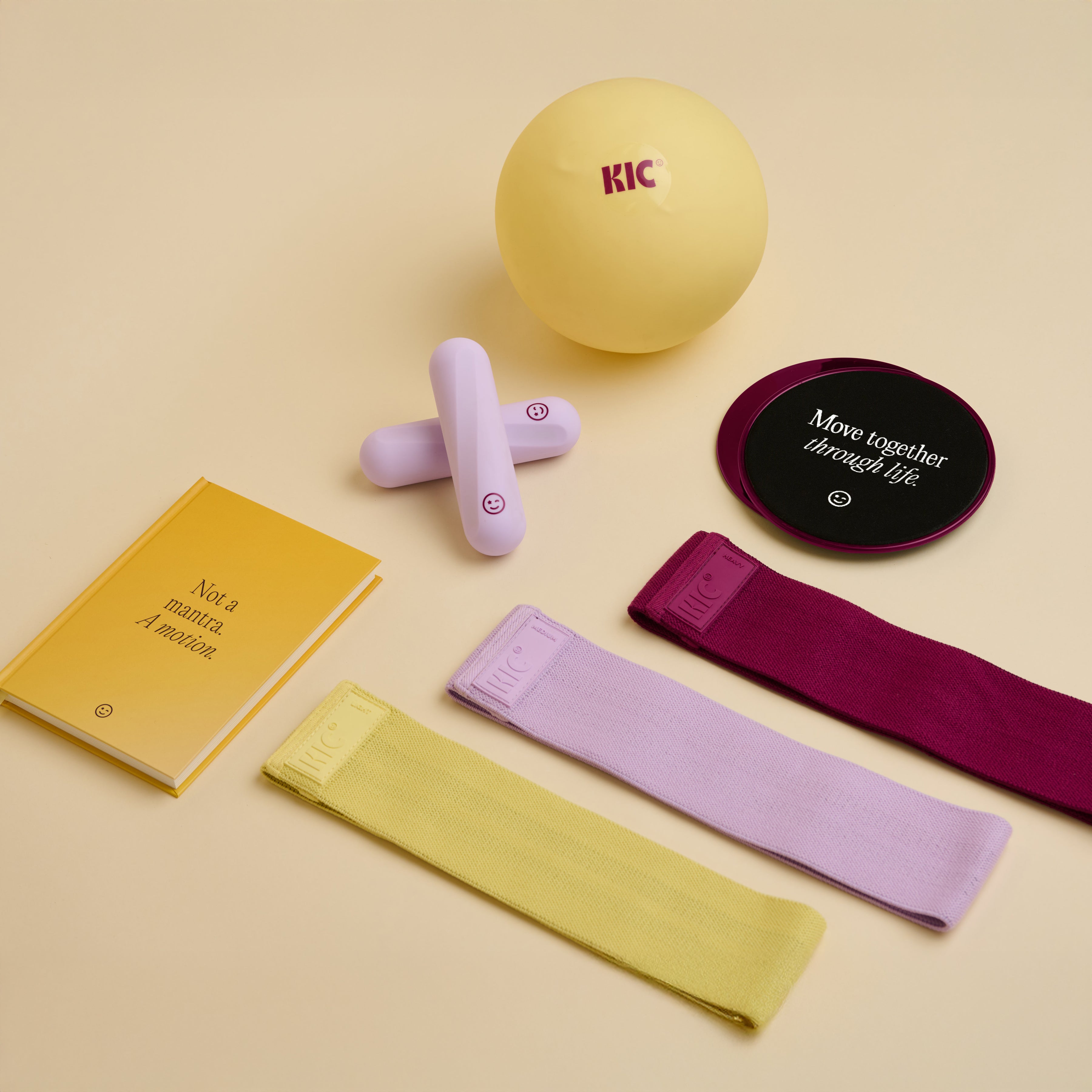 Collection of fitness items including a yellow ball, resistance bands, and a notebook on a beige background.