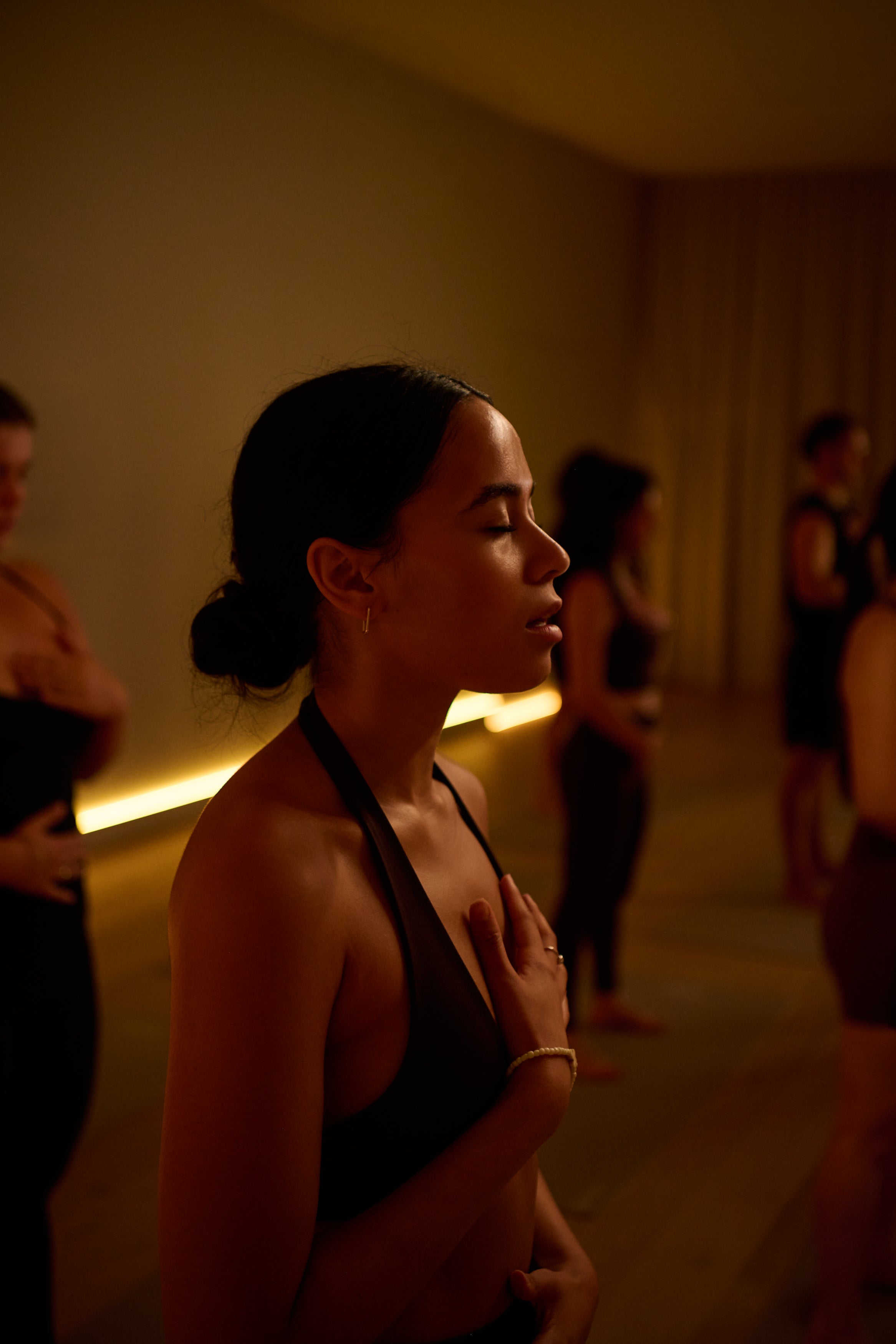Woman in a black activewear standing in a dimly lit KICStudio class doing breathing exercises