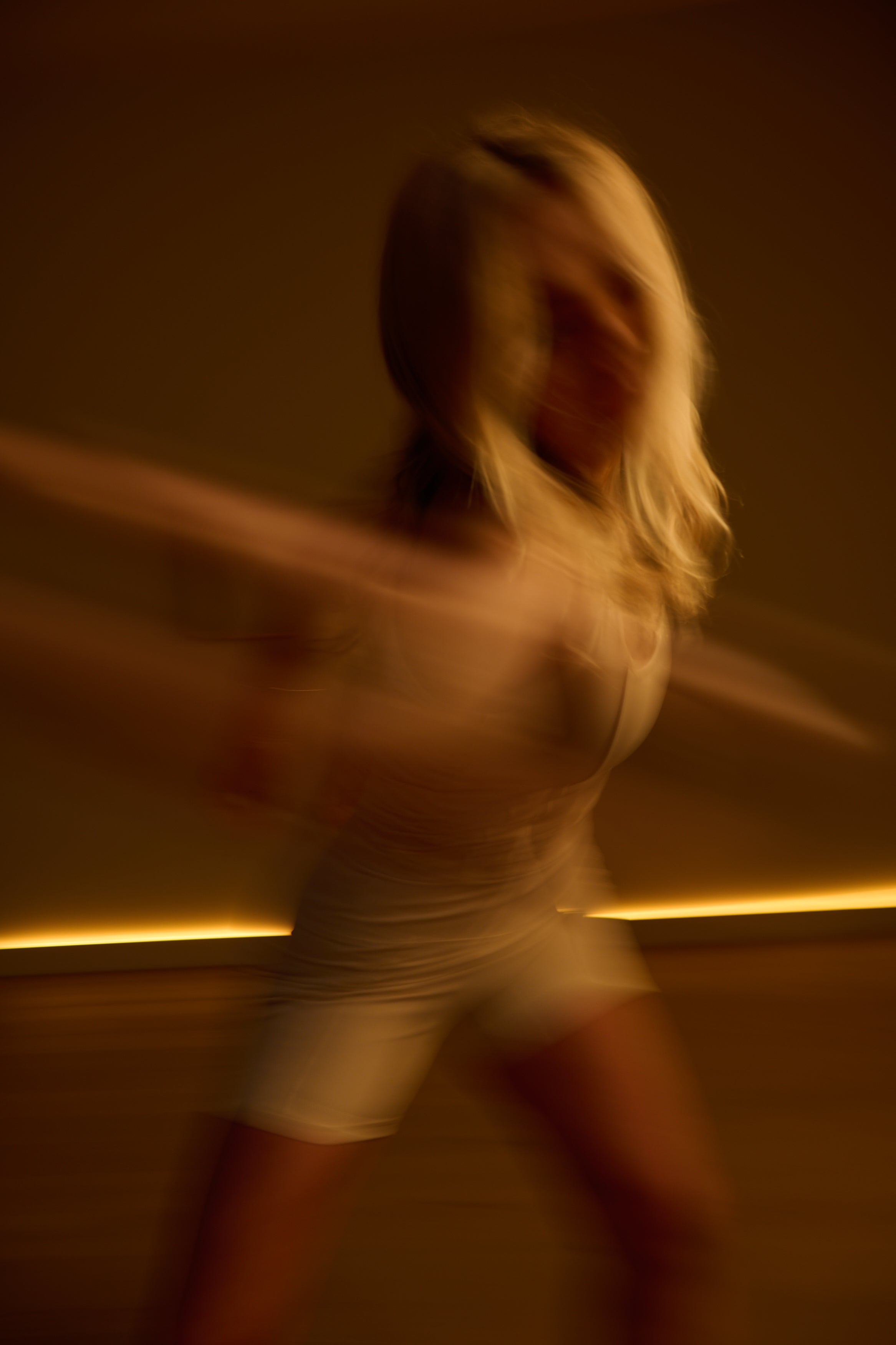 Person in white activewear with arms outstretched against a warm-toned wall.