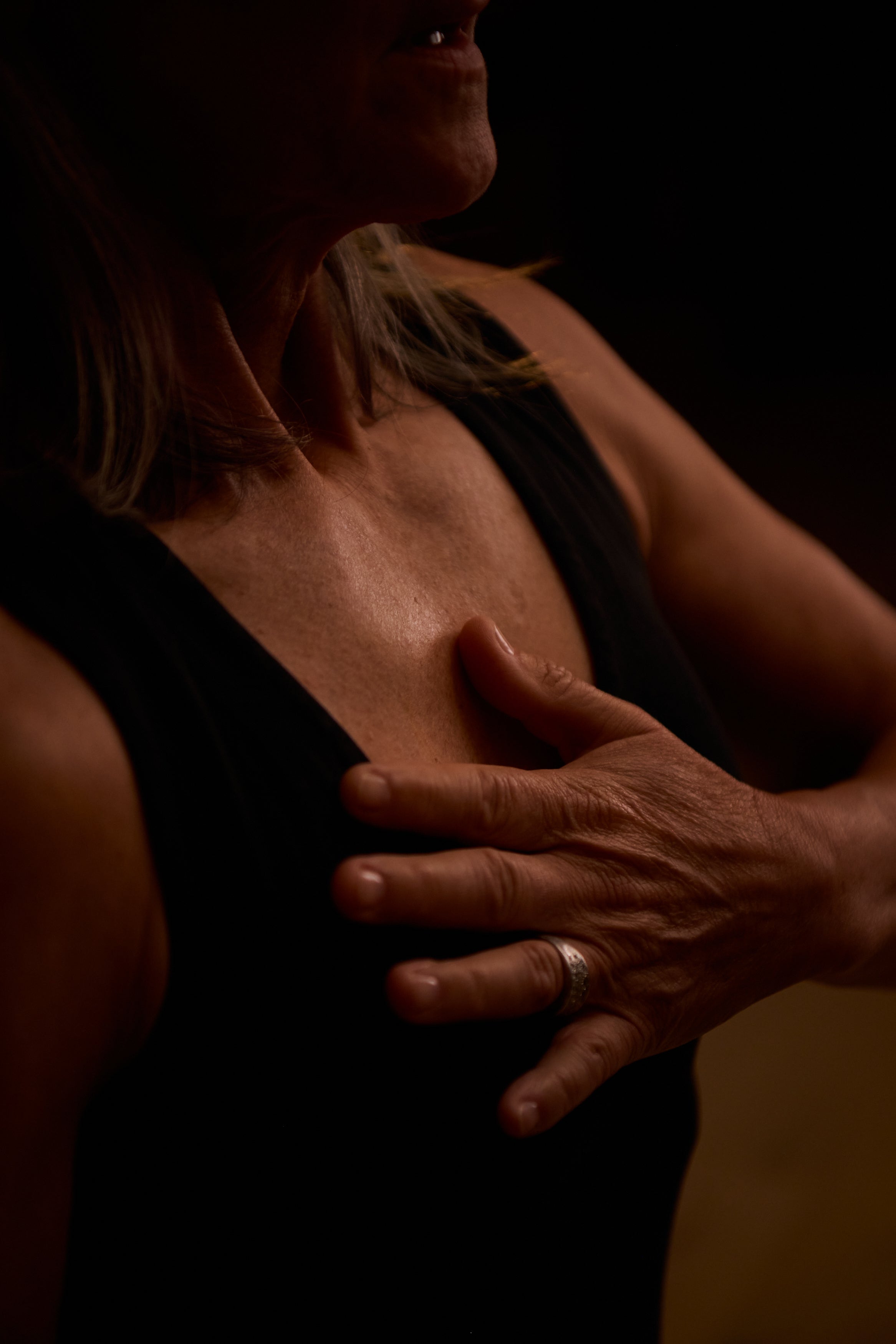 Woman with a hand on her chest against a dark background