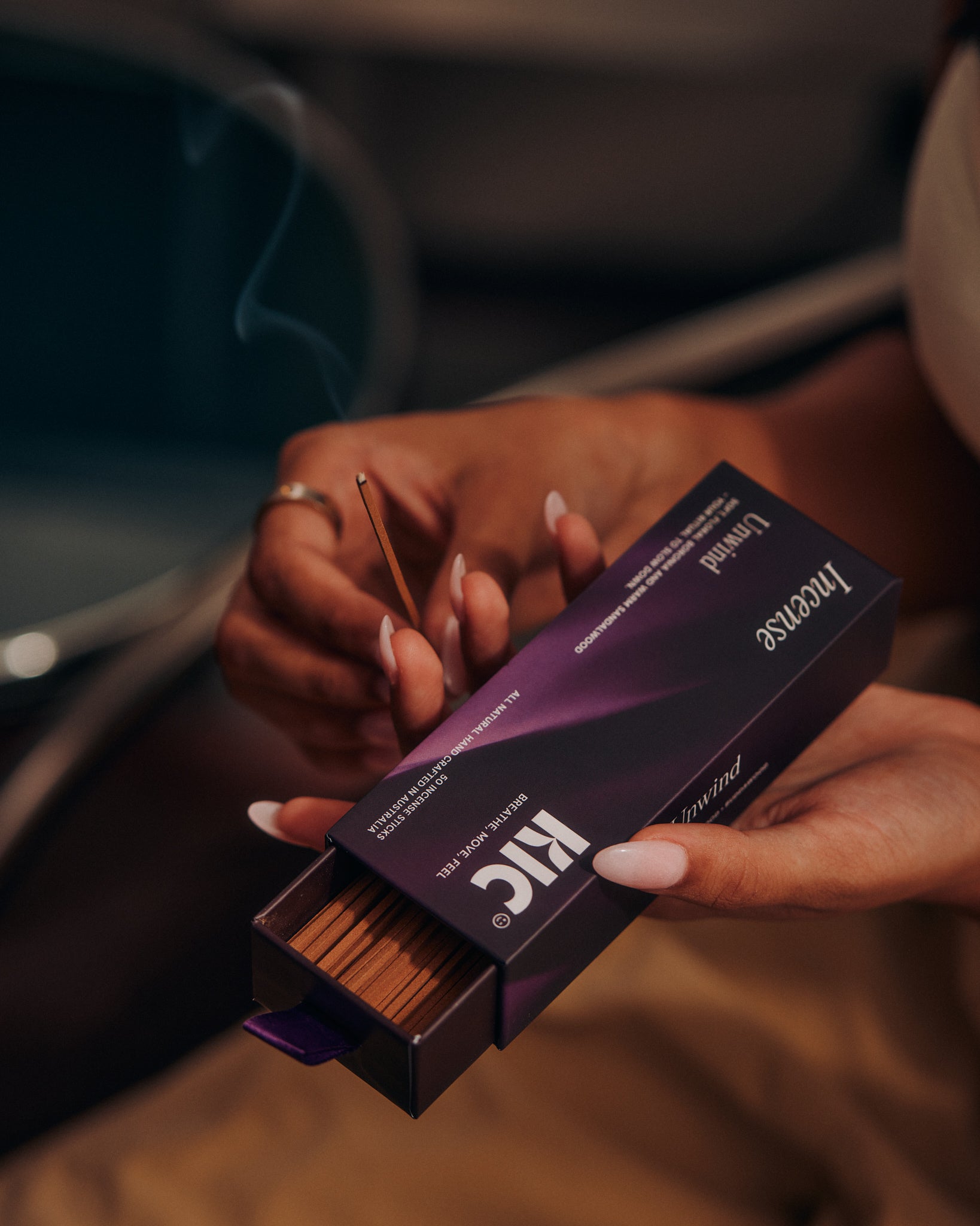 Women holding KIC's Unwind Incense in hands with stick burning. 