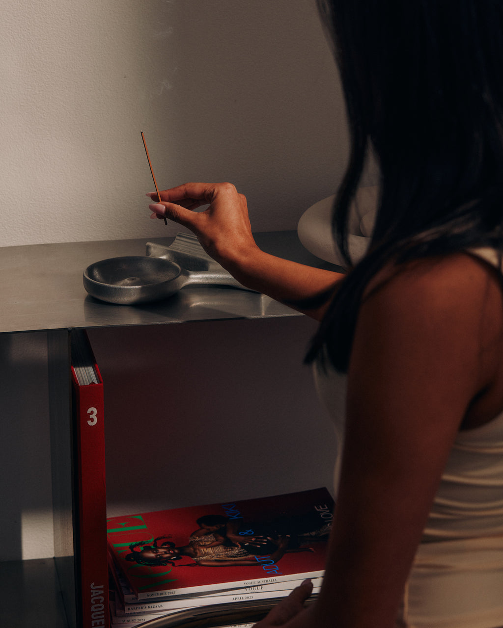 Woman placing a KIC incense stick in a holder beside books
