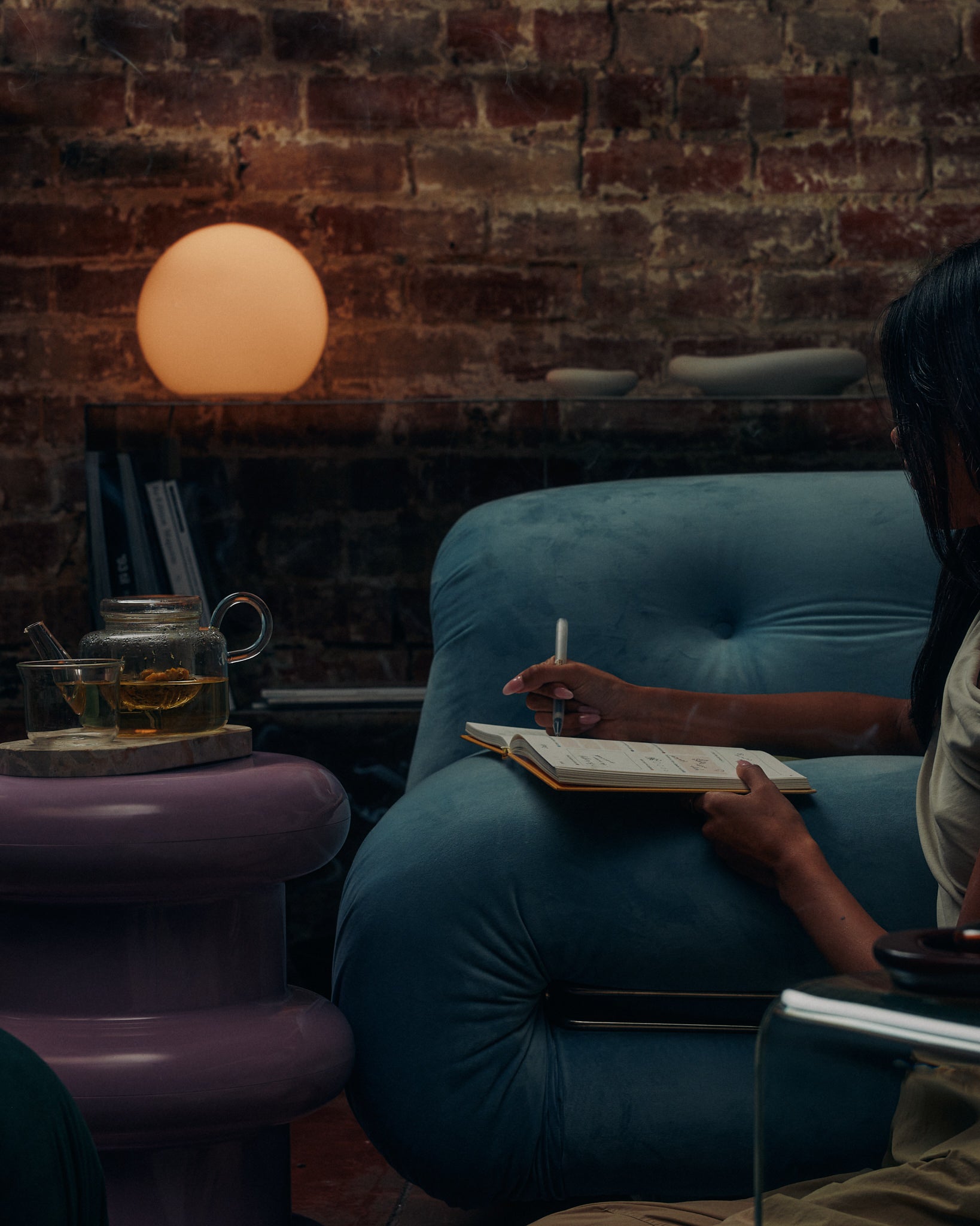 Woman journaling in an armchair beside KIC tea and incense