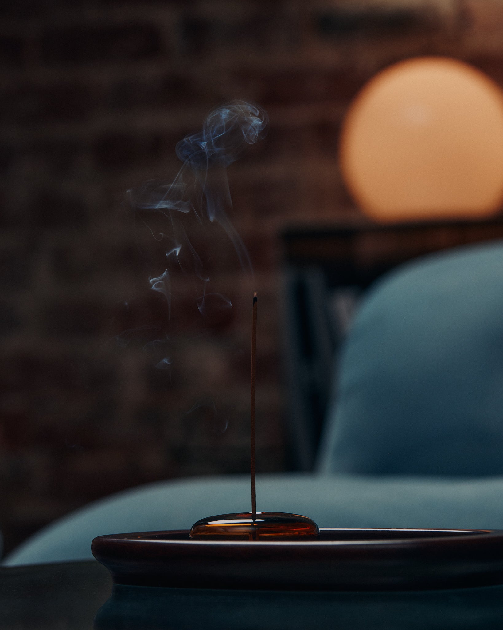 KIC incense stick smoking on a tray beside a velvet armchair