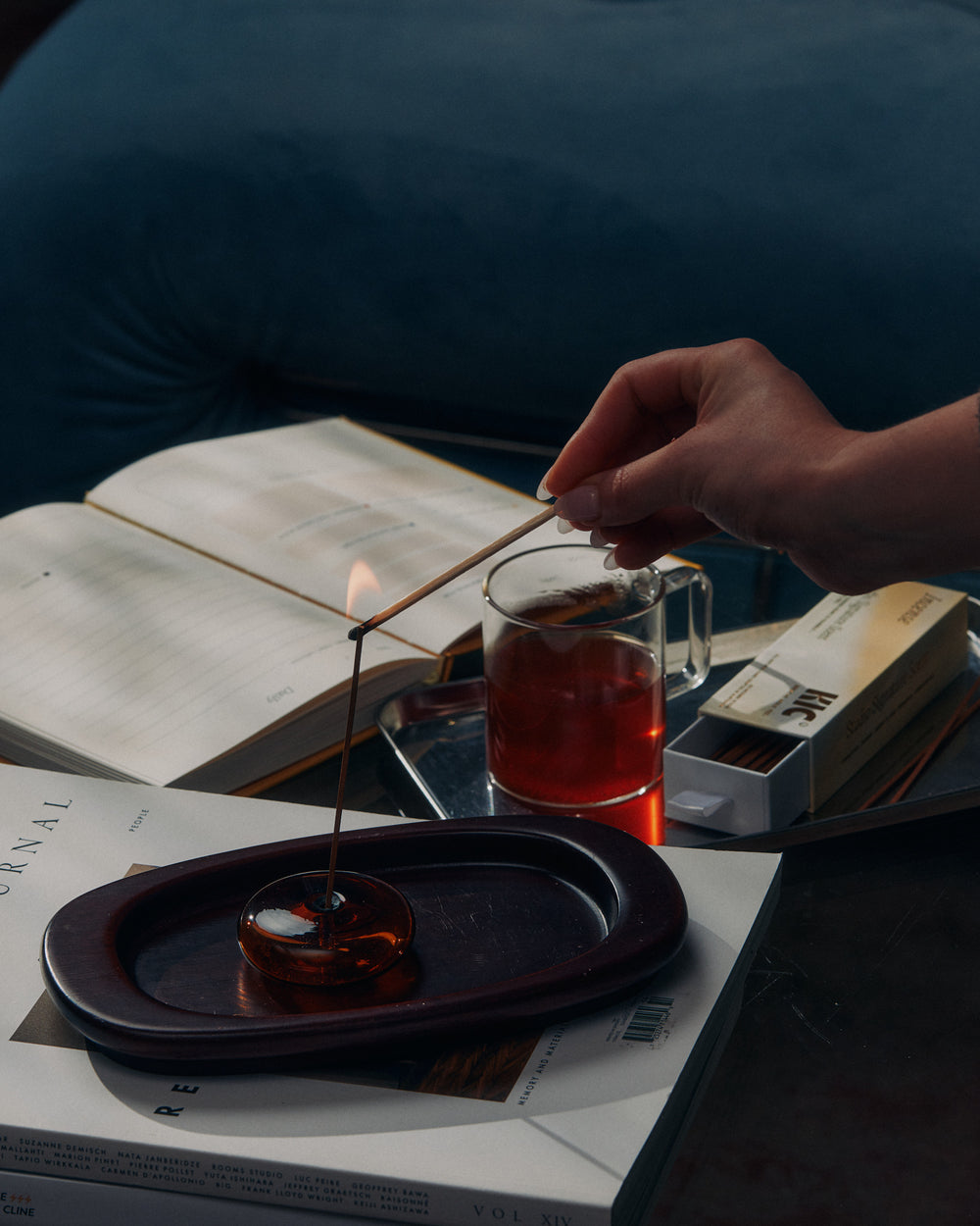 Woman lighting a KIC incense stick beside tea and a goals journal