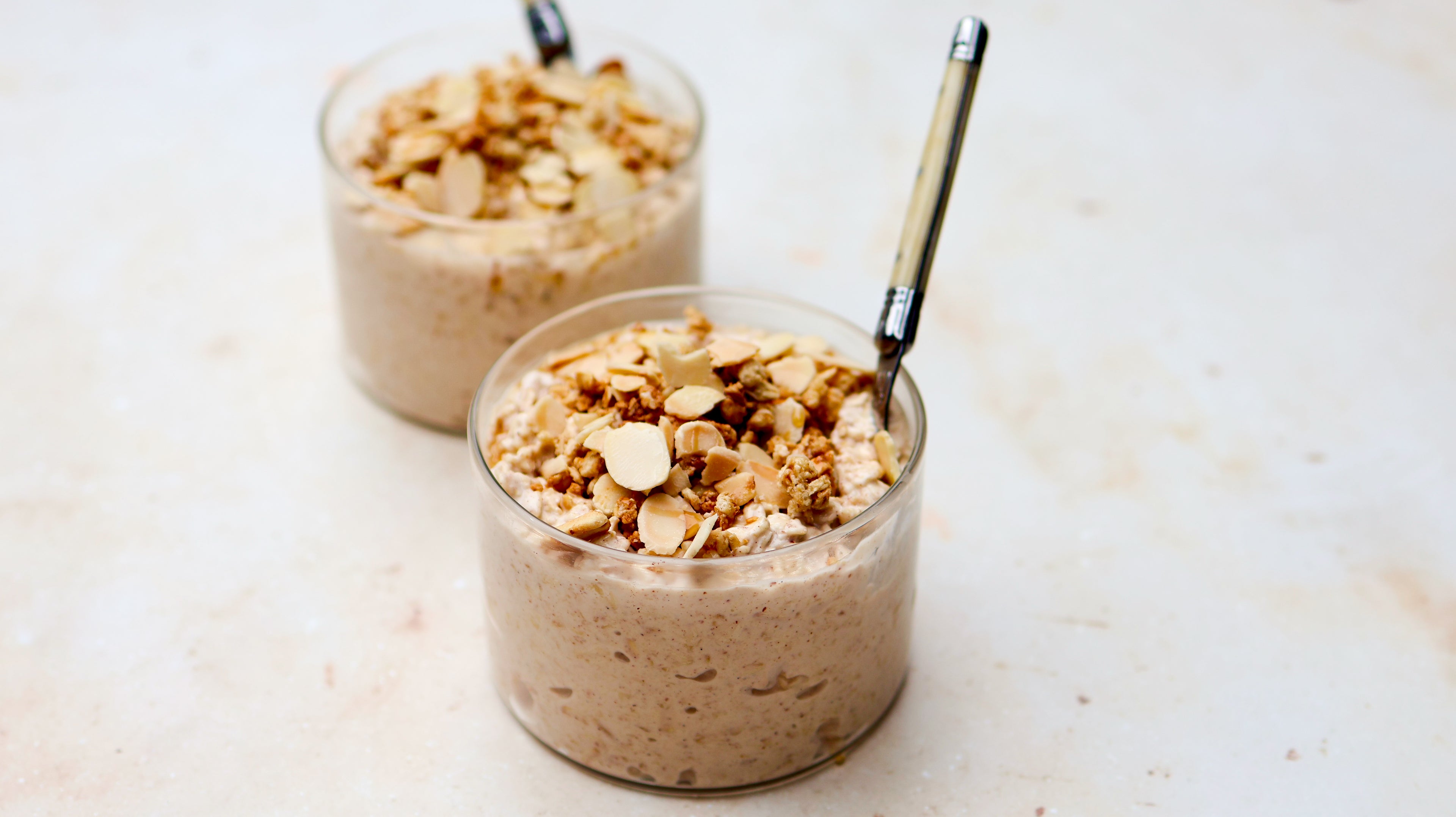Two glass jars filled with a creamy overnight oats topped with nuts on a light background