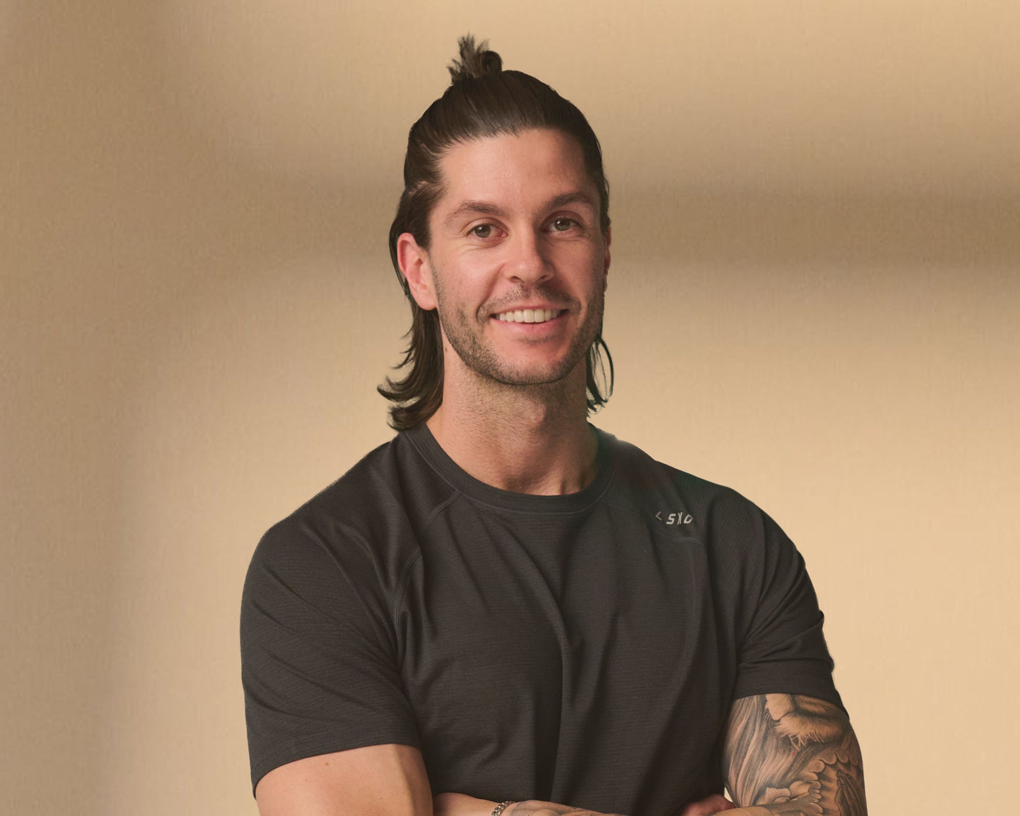 Man with a beard and tattoo wearing a black t-shirt against a beige background