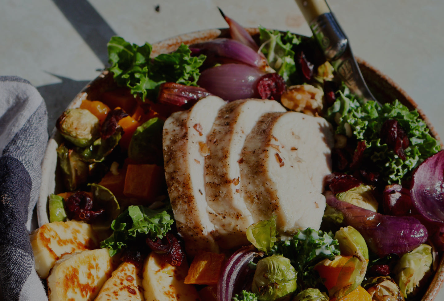 Salad with chicken, vegetables, and a fork on a stone surface