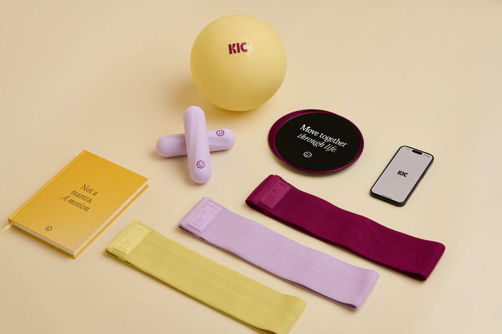 Collection of fitness items including resistance bands, a ball, and phone on a beige background
