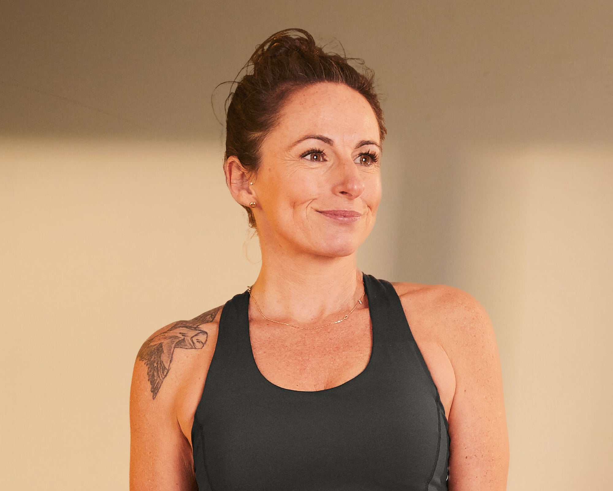 Karen is a woman with brown hair smiling beyond the camera with a tattoo on her shoulder