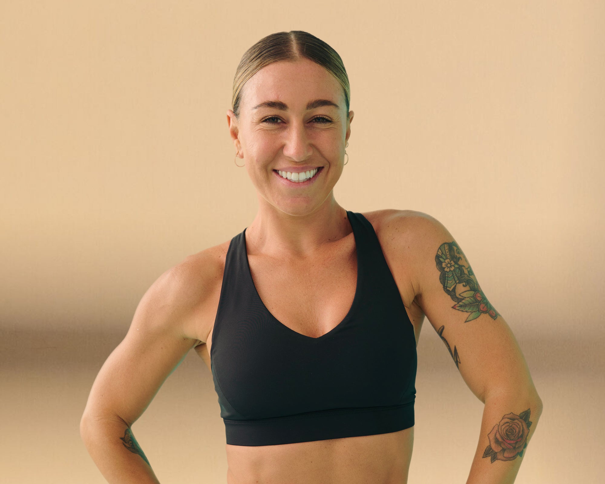 Kika a woman with hair tied up smiling with a black sports bra and tattoos on her arms