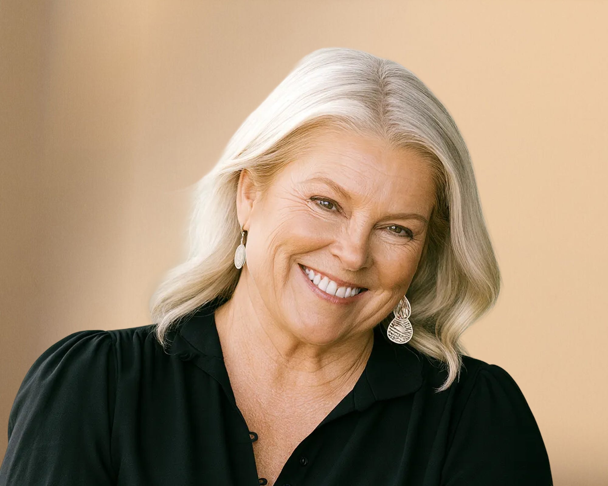Lael with platinum blonde-grey hair and silver earrings, smiling at the camera in a black top