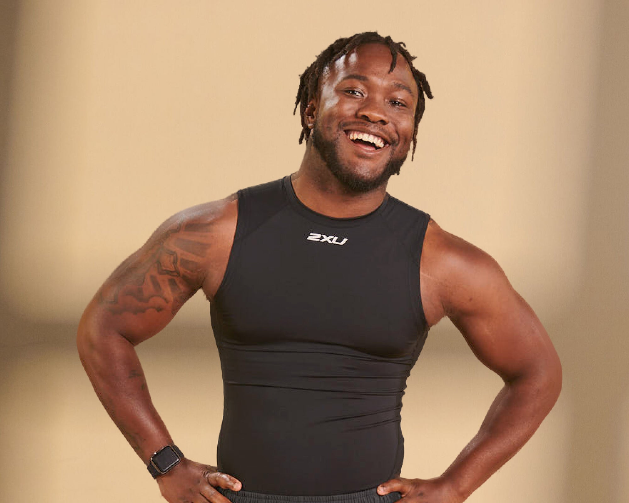 Leo a man with black curly hair smiling at the camera with tattooed arms and black 2XU top
