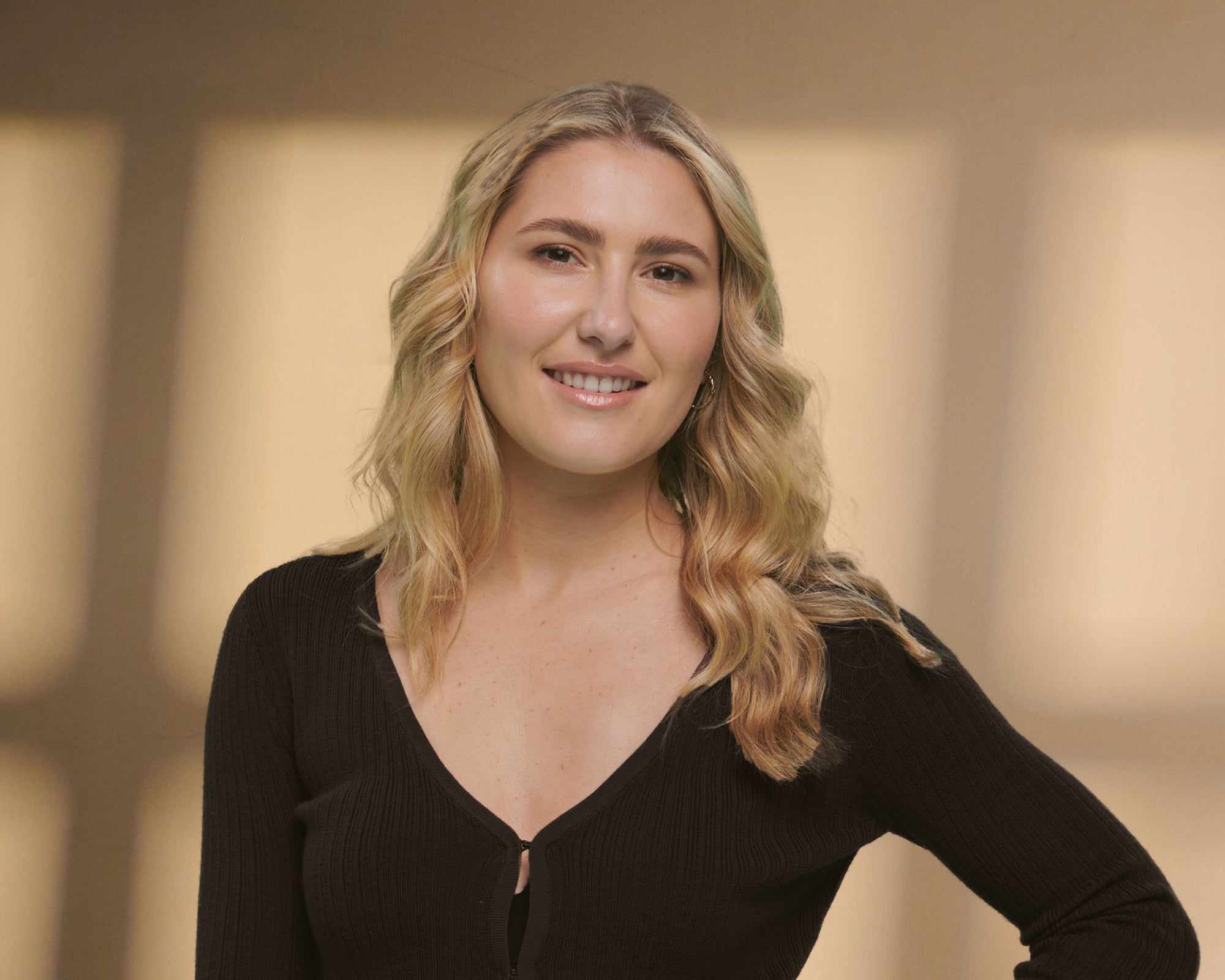 Woman with blonde hair wearing a black top against a warm-toned background