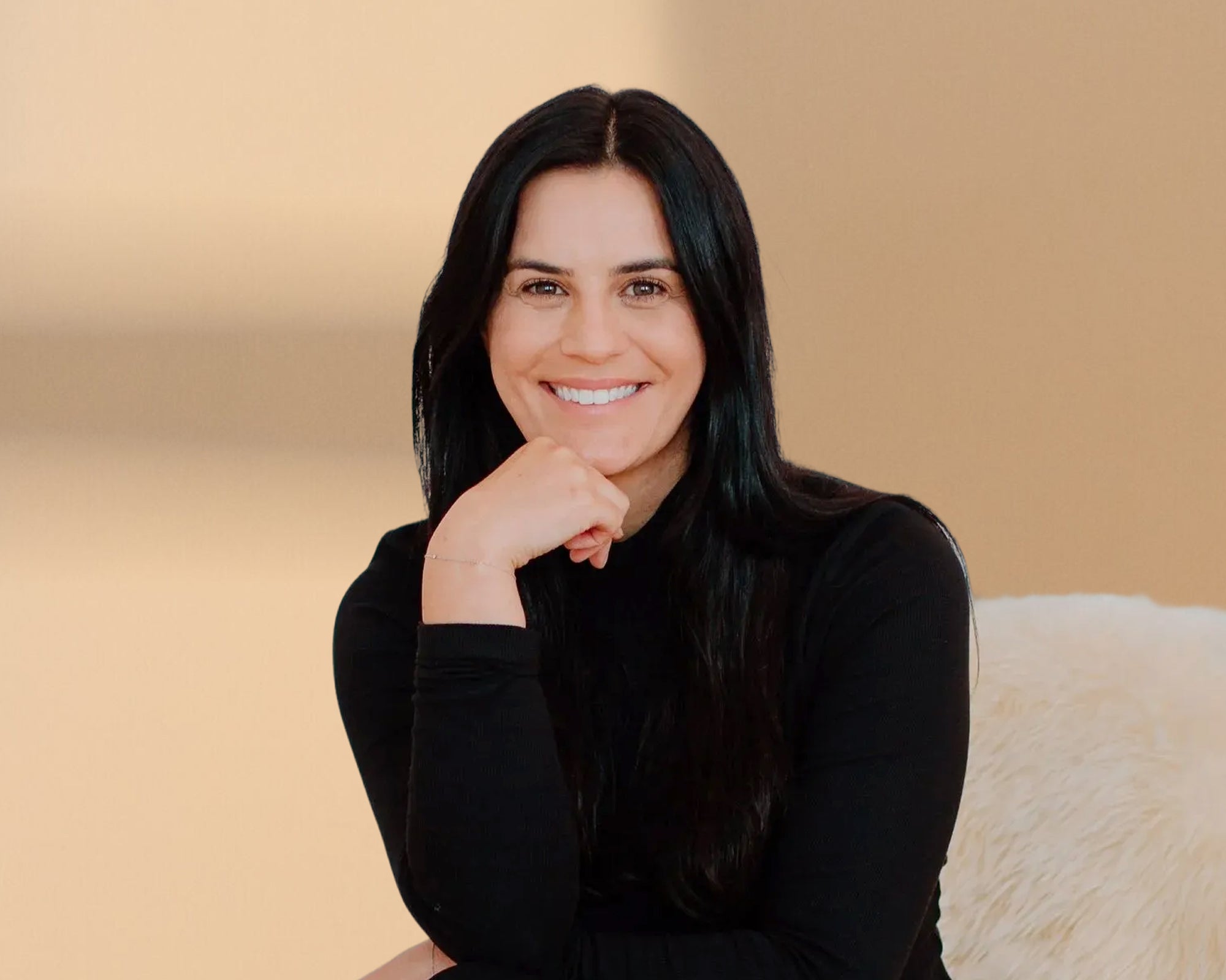 Woman with long dark hair wearing a black top against a beige background