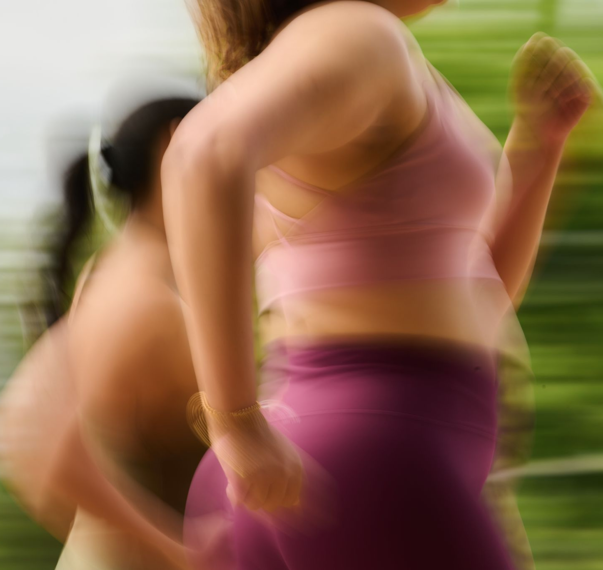 Person in pink top and purple leggings exercising outdoors with a blurred background