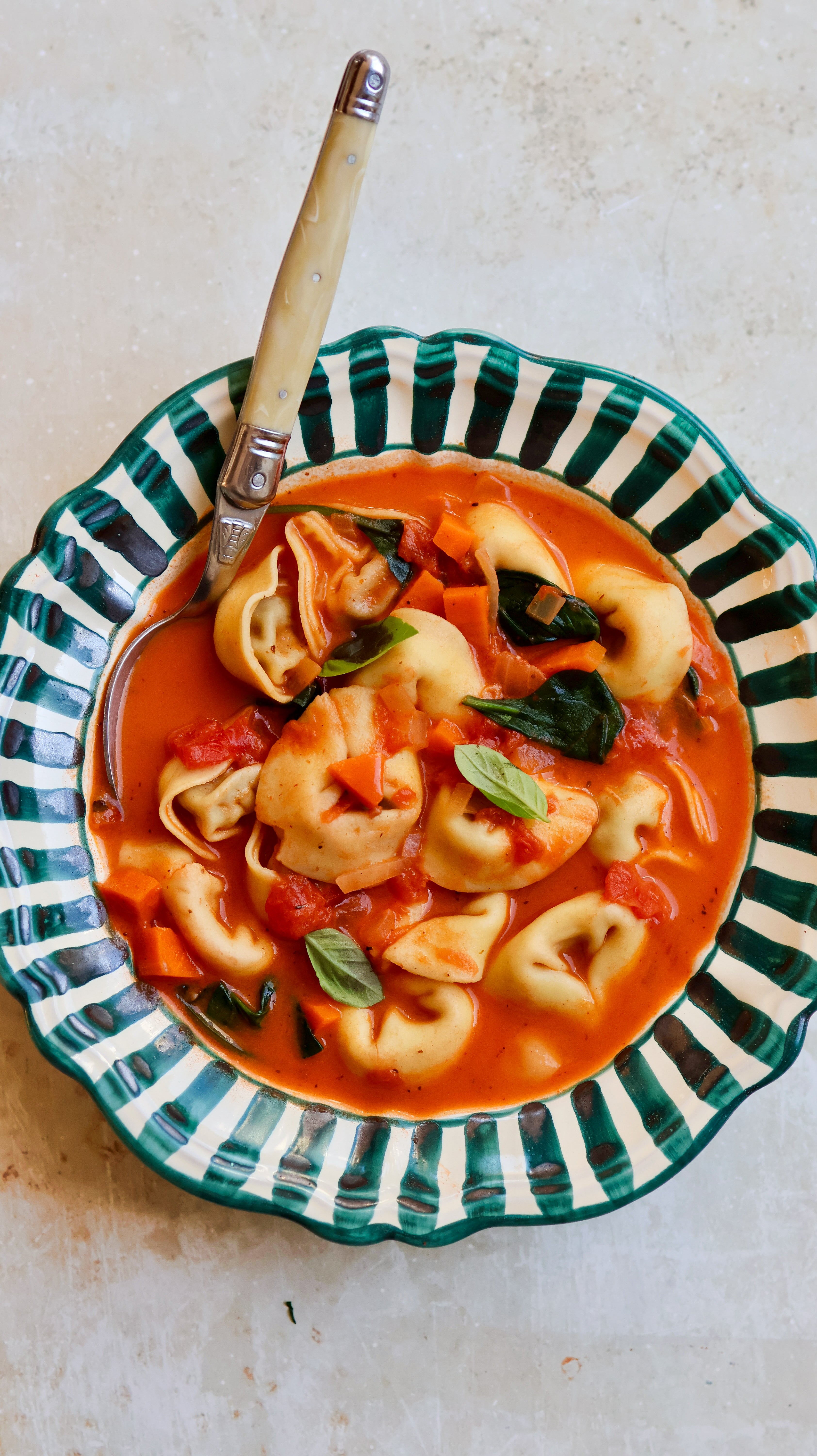Tortellini soup in a decorative bowl with a spoon on a light background