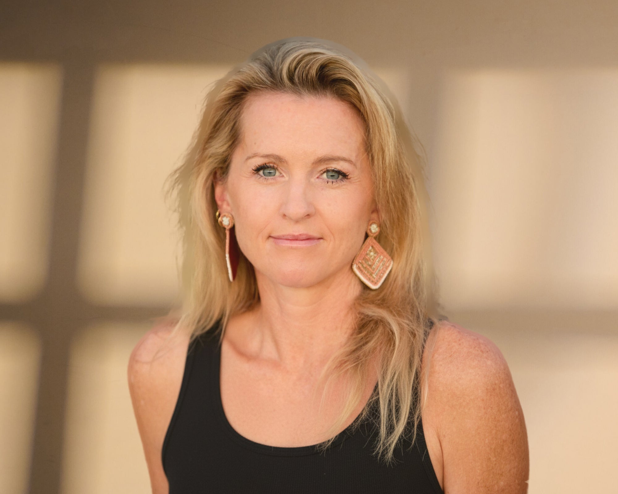 A picture of Tina with blonde hair and earrings wearing a black top against a blurred background