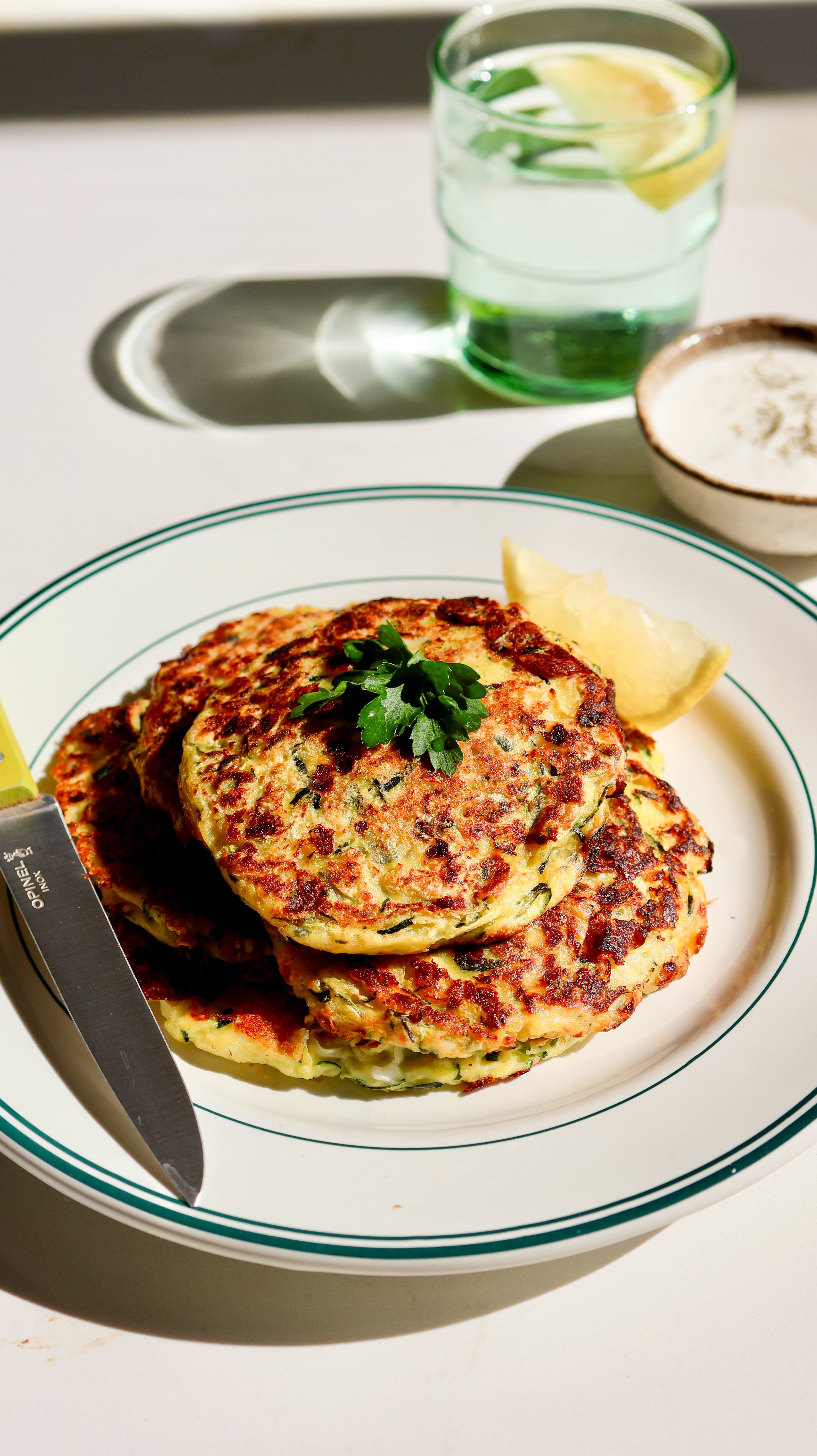 Zucchini fritters on a plate with a glass of water and lemon slices in the background.