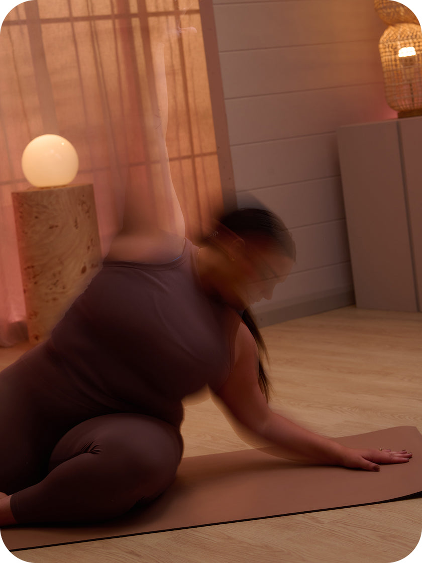 Person stretching on a mat in a dimly lit room with soft lighting.