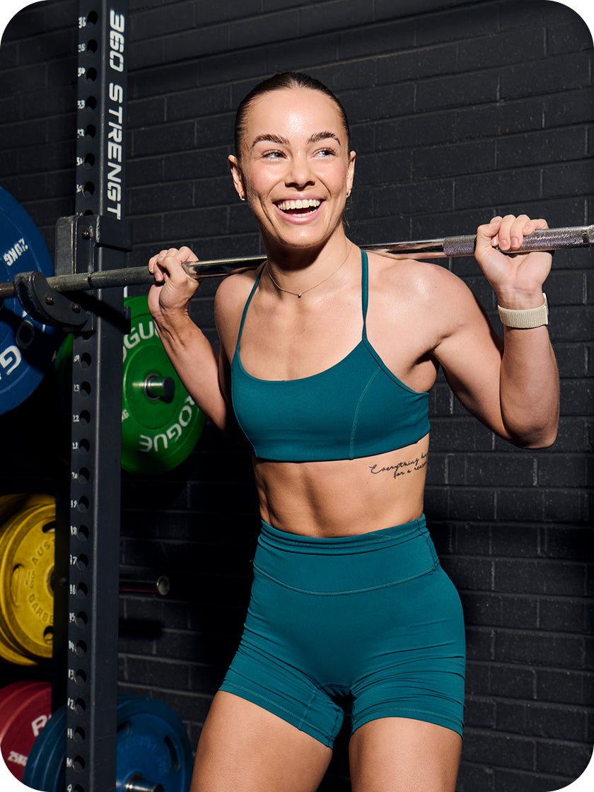 Woman in teal athletic wear lifting a barbell in a gym setting