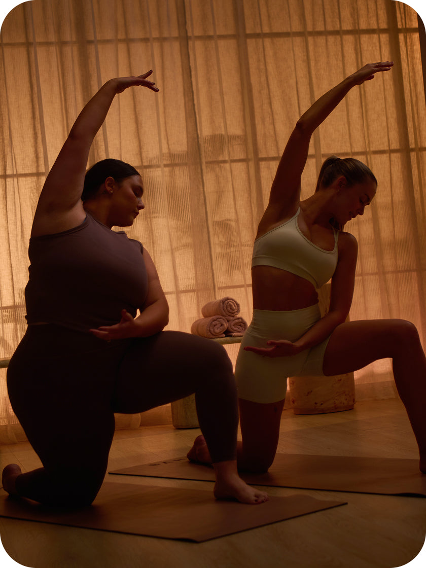Two women practicing yoga in a dimly lit room with warm lighting.