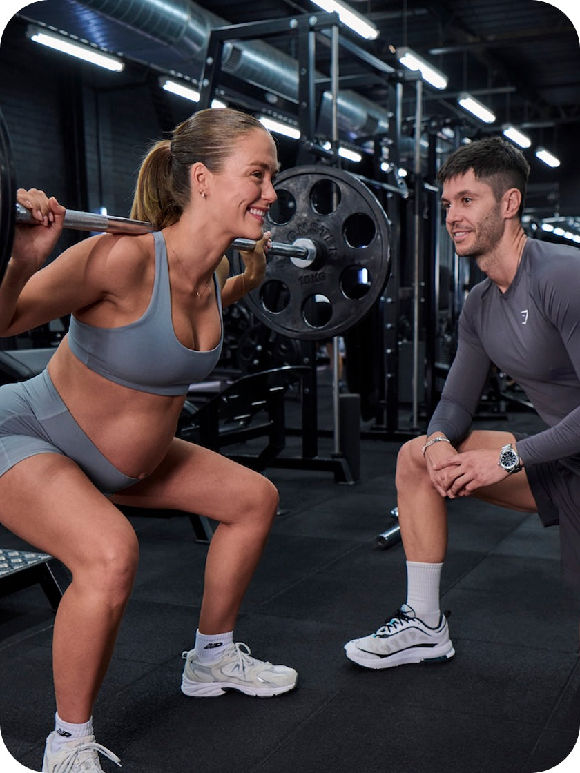 Pregnant woman performing squats with a spotter in a gym setting