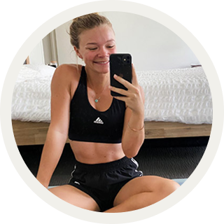 Woman in black athletic wear using a phone in front a bed